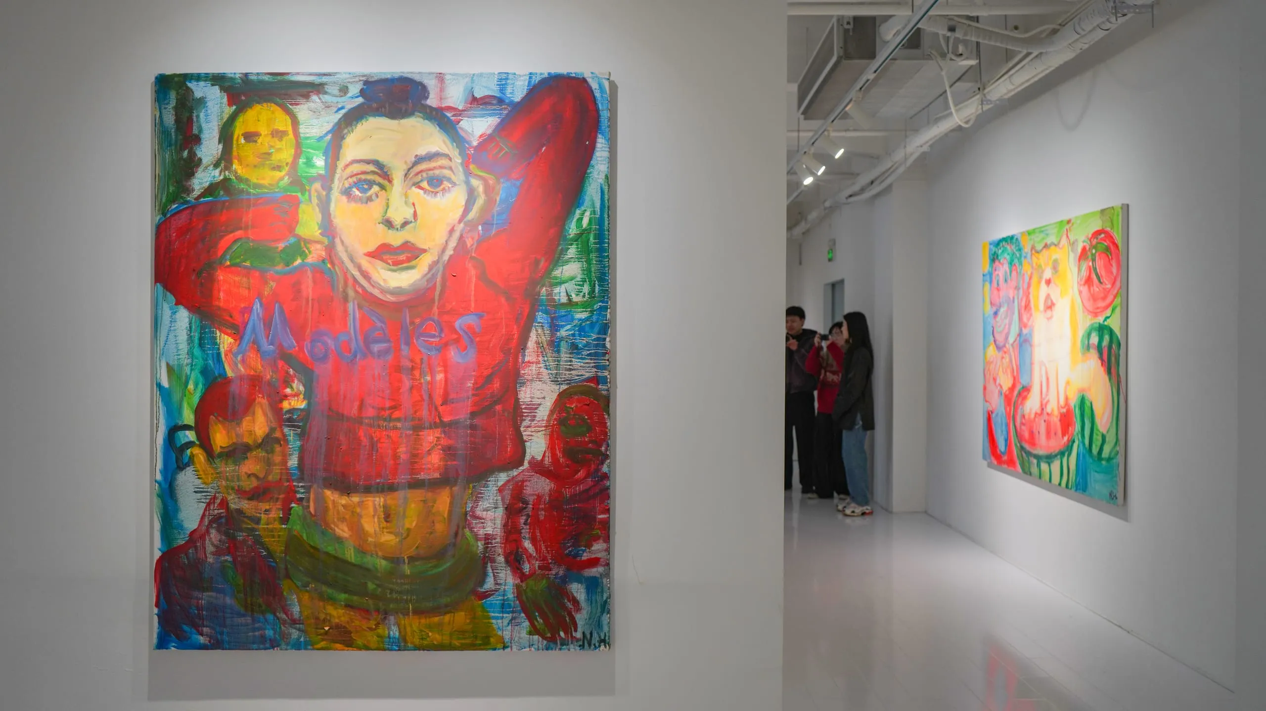 A tall red-jacketed portrait at the end of a corridor, visitors gathered before further canvases.