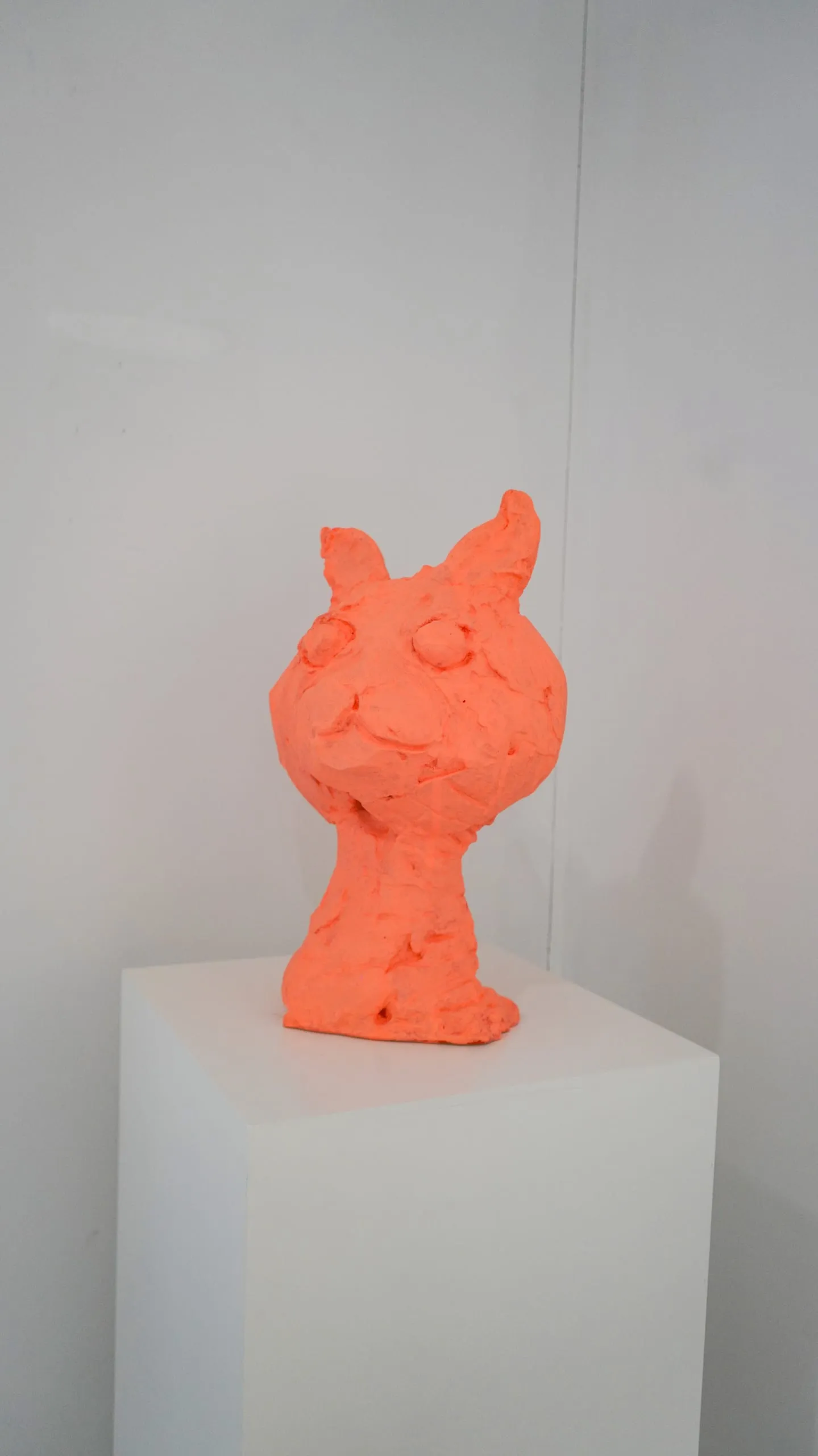 A coral-orange cat bust on a white plinth.